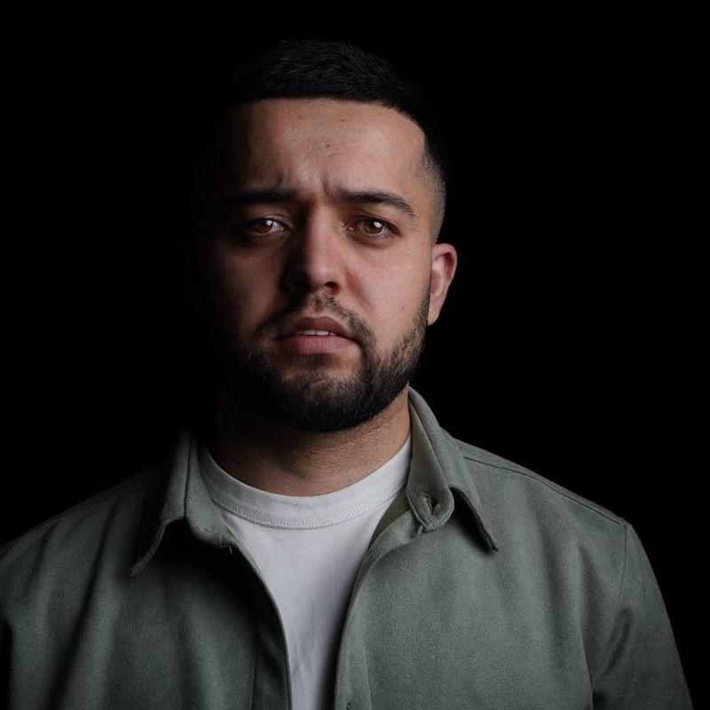 Man in a focused stance preparing for a bodyweight squat in a dark studio.